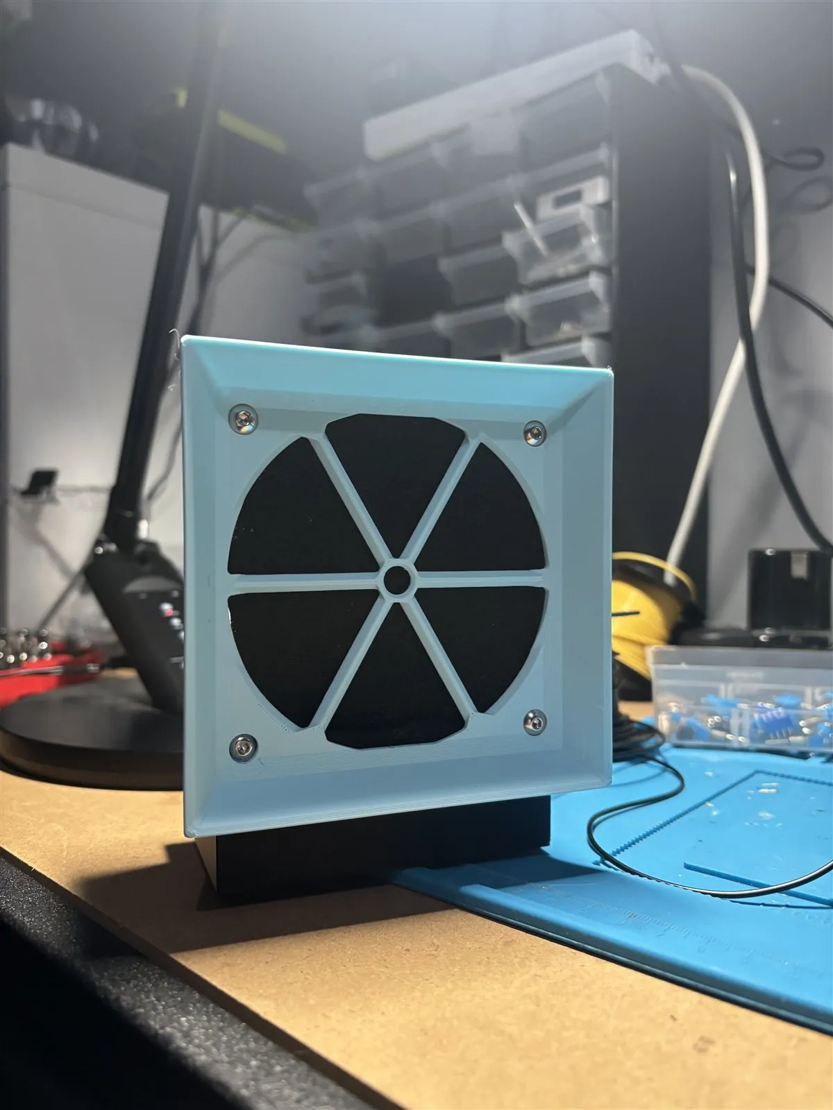 Blue 3D-printed bench fume extractor with a square front grille on an electronics workbench