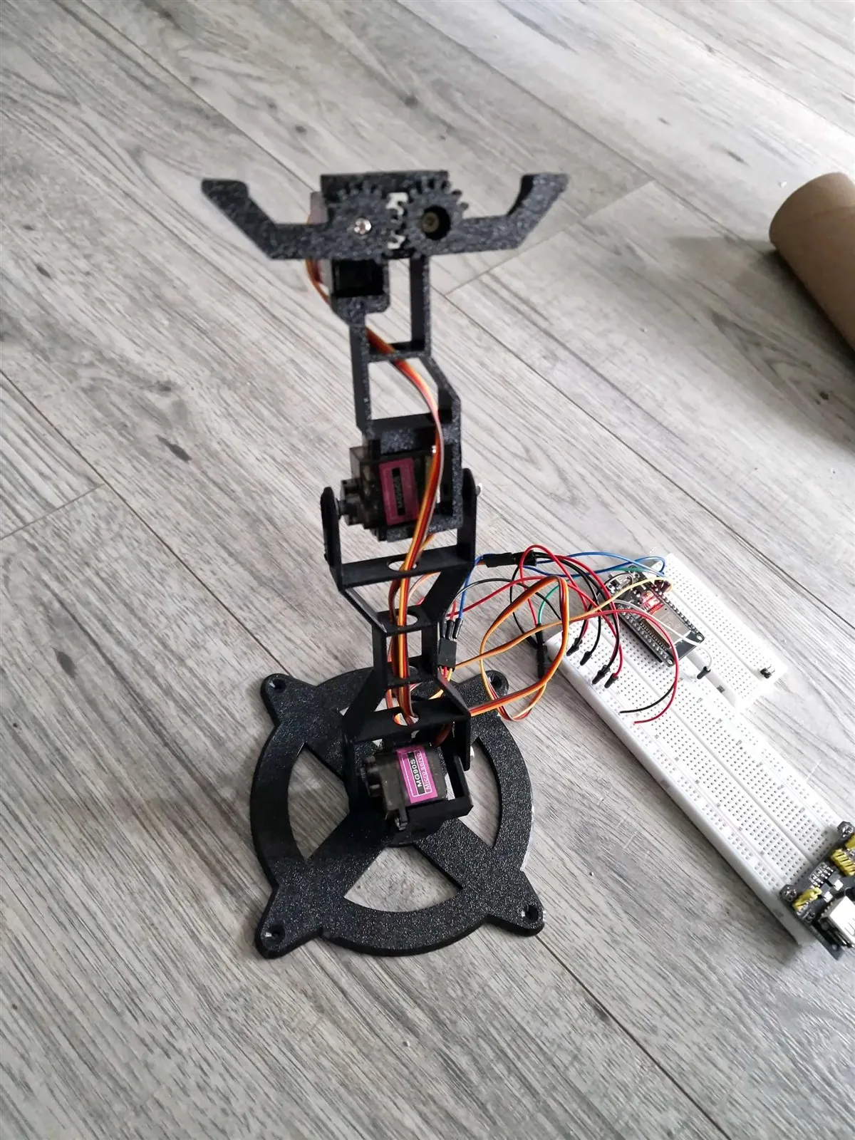 Servo Mini Arm on a floor beside its breadboard joystick-control circuit